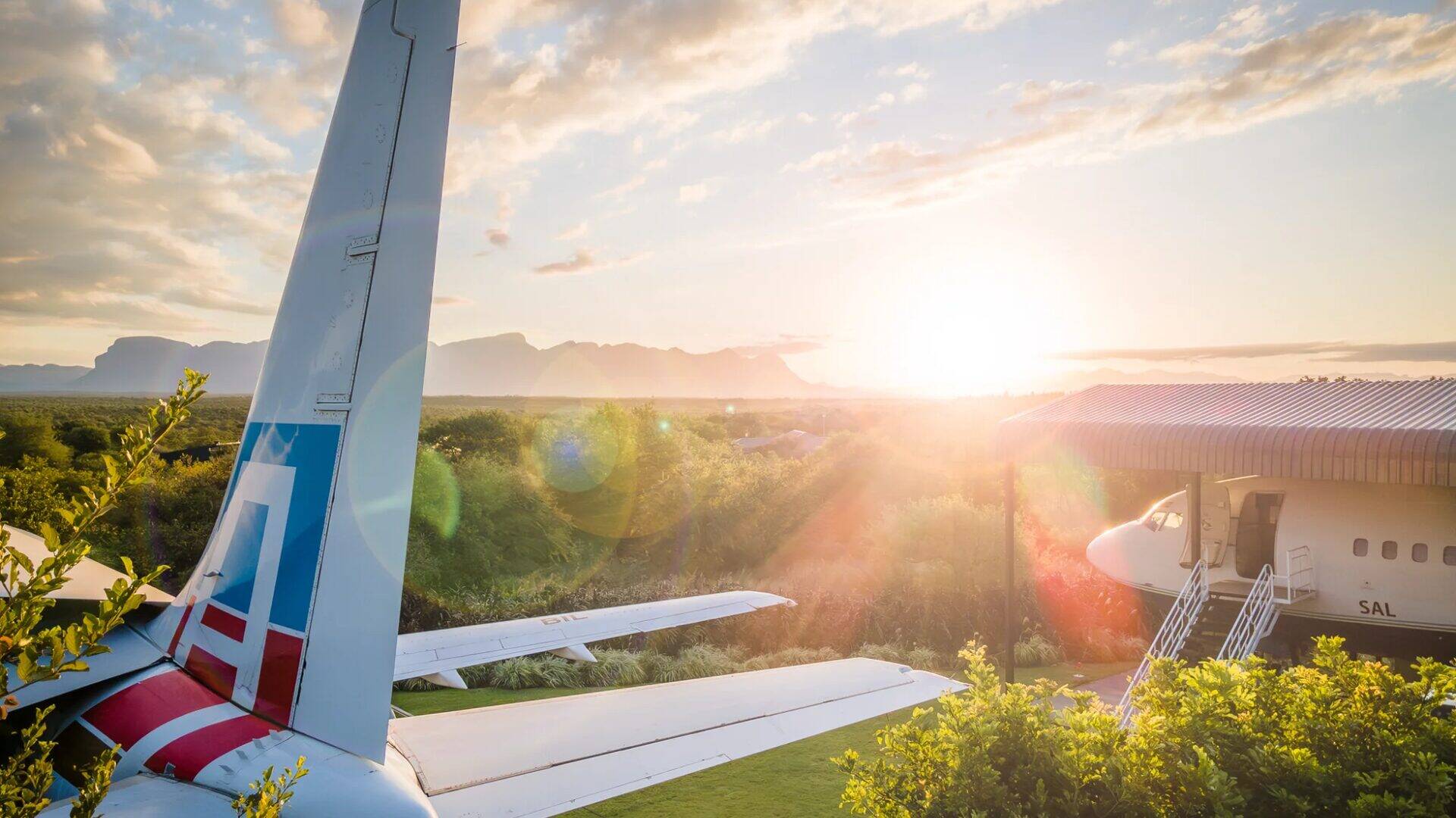 Sunset view of Aerotel aircraft with Drakensberg mountains in background, showing Boeing 737 tail and entrance stairs